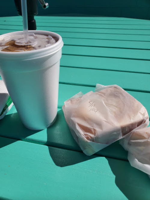 A white cup with a straw next to two wrapped sandwiches on a turquoise table.