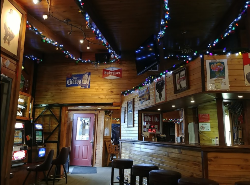 Cozy bar interior with wooden walls, colorful lights, slot machines, and a red door.