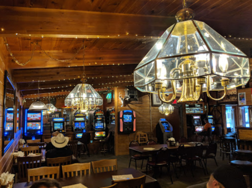 Cozy interior of a rustic casino with slot machines, wooden decor, and warm lighting from large chandeliers.