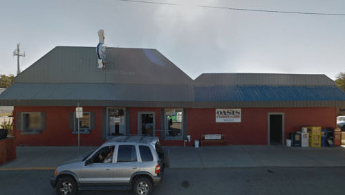 A red building with a gray roof, featuring a sign for "Oasis" and a cartoon fish on top, with a parked SUV in front.