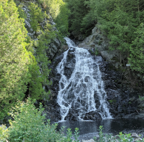 A serene waterfall cascading down rocky cliffs, surrounded by lush green trees and a calm pool below.