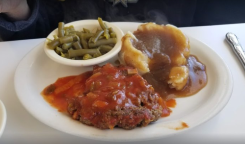 A plate with meatloaf topped with sauce, mashed potatoes with gravy, and a side of green beans.