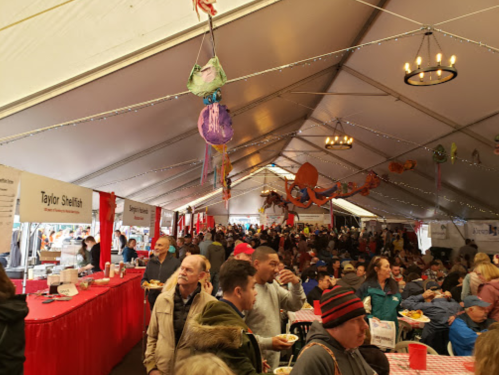 A crowded tent filled with people enjoying food at a festive event, with colorful decorations overhead.