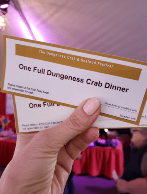 A hand holding two tickets for a Dungeness Crab Dinner at the Dungeness Crab & Seafood Festival.