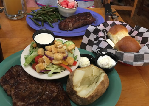 A hearty meal featuring a steak, baked potato, salad, green beans, and rolls on a wooden table.