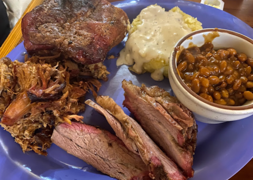 A blue plate with various meats, including pulled pork, brisket, and a side of baked beans and creamy mashed potatoes.