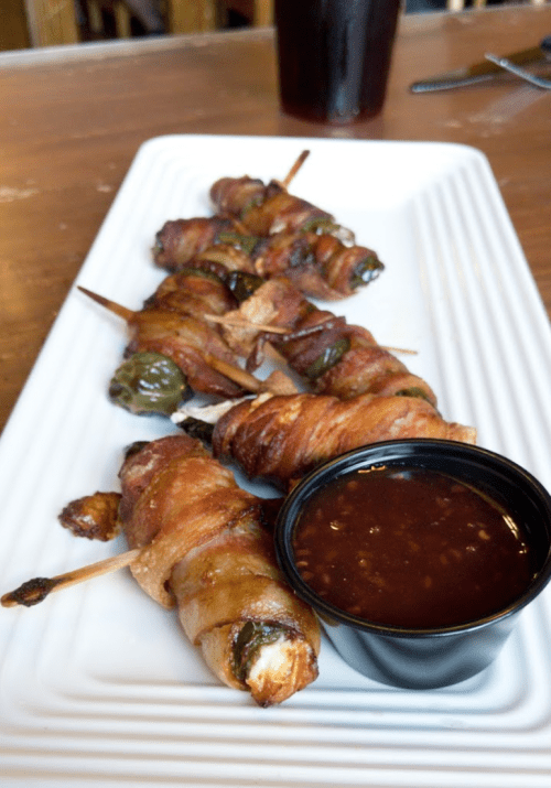 A platter of bacon-wrapped jalapeño poppers served with a small bowl of dipping sauce.