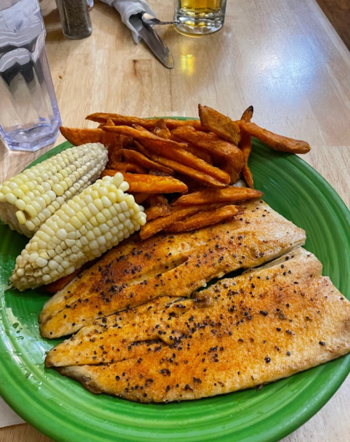 A green plate with seasoned fish fillets, sweet potato fries, and corn on the cob.