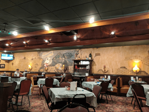 Cozy restaurant interior with checkered tablecloths, wooden accents, and a mural on the wall.