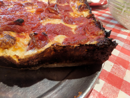 Close-up of a crispy, pepperoni-topped pizza with a charred crust on a checkered tablecloth.