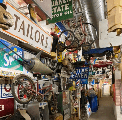 A colorful display of vintage signs, bicycles, and toys hanging in a narrow, eclectic hallway.