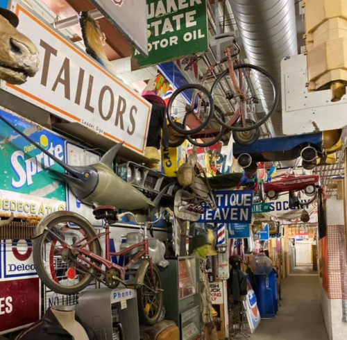A colorful display of vintage signs, bicycles, and toys hanging in a narrow, eclectic hallway.