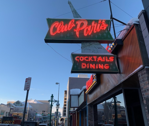 Neon sign for "Club Paris" featuring "Cocktails" and "Dining" against a clear blue sky. Snow on the ground.