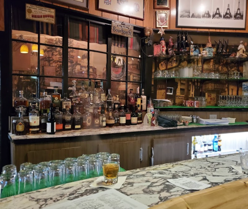 A cozy bar with a marble countertop, shelves lined with various liquor bottles, and a warm, inviting atmosphere.