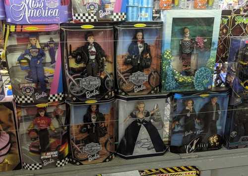 A display of various Barbie dolls in themed packaging, featuring different outfits and accessories.