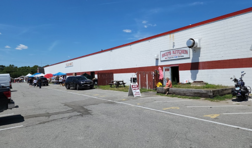 A parking lot with cars and a building labeled "Crisp's Butcher" next to a market with tents and people.