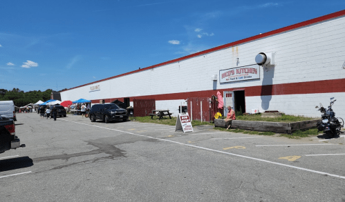 A parking lot with cars and a building labeled "Crisp's Butcher" next to a market with tents and people.