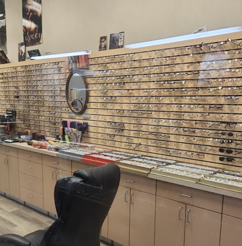 A display of various eyeglasses and sunglasses on a wooden wall, with a black chair in front and a mirror on the side.