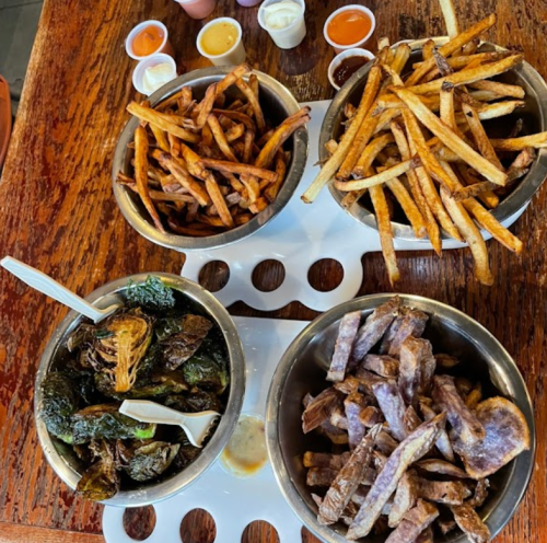 Three bowls of fries: sweet potato, regular, and a green vegetable mix, with various dipping sauces on the side.