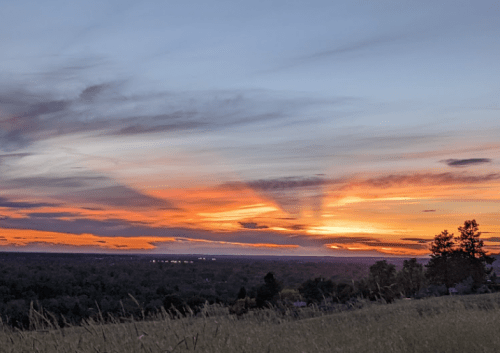 A vibrant sunset with orange and purple hues over a landscape, casting long shadows across the horizon.