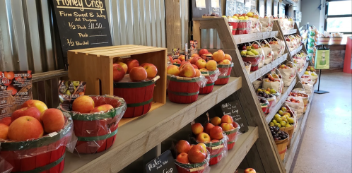 A market display featuring baskets of apples and various fruits on wooden shelves, with chalkboard signs.