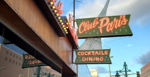 Neon signs for "Club Paris" and "Cocktails Dining" against a cloudy sky, showcasing vintage-style lettering.