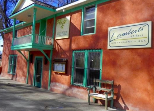 Exterior of Lambert's of Taos restaurant, featuring a peach-colored building with green accents and a wooden bench.