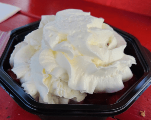 A black container filled with a mound of whipped cream on a red table.