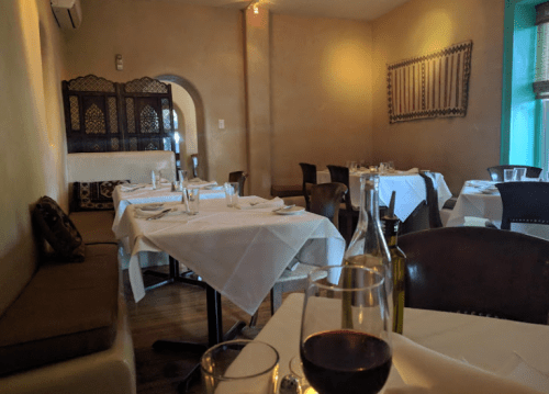 A cozy restaurant interior with white tablecloths, wine bottles, and a warm ambiance.