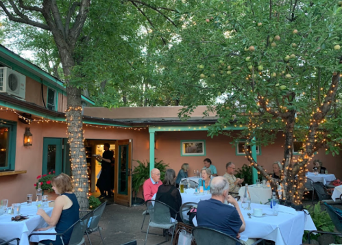 Outdoor dining area with tables, string lights, and a tree with fruit, filled with patrons enjoying their meals.