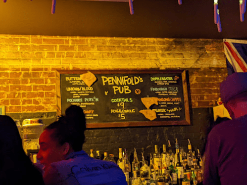 A dimly lit bar with a chalkboard menu listing cocktails and non-alcoholic drinks at Pennifold's Pub.