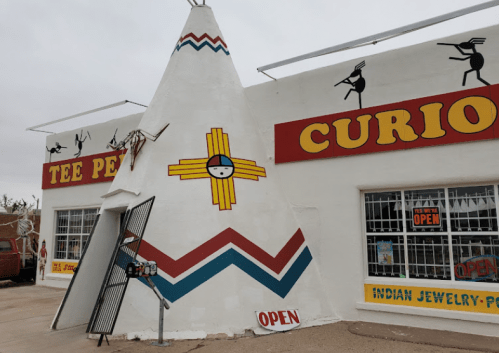 A colorful teepee-shaped building with "Curios" and "Open" signs, featuring Native American designs and jewelry displays.