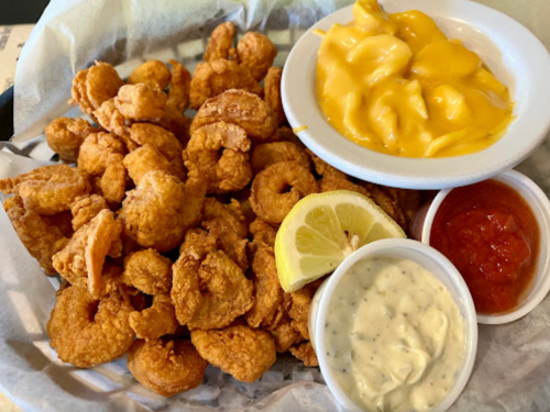 A basket of crispy fried shrimp with lemon, served with two dipping sauces and a bowl of macaroni and cheese.