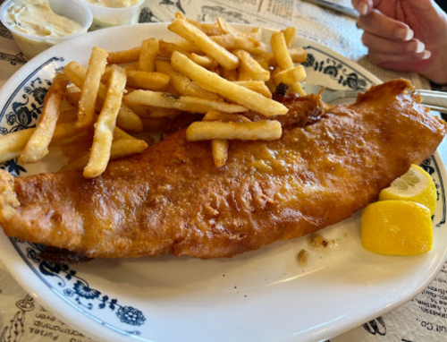 A plate of golden-brown fried fish with crispy fries and lemon wedges, served on a decorative dish.