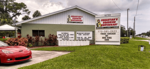 Sign for Sebastian's Roadside Restaurant, featuring specials for fried chicken and BBQ ribs, with a red car parked outside.