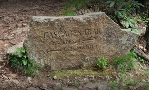 A weathered stone sign marking the Cascades Trail, with directions to Cascades and Parking Lot.