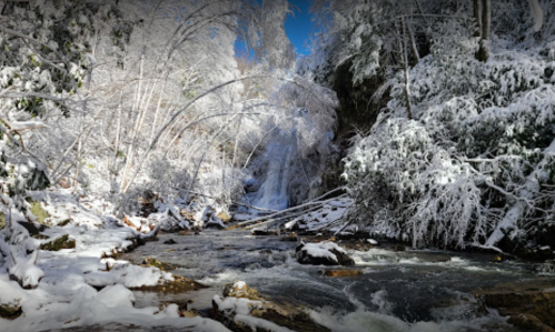 A serene winter landscape featuring a snowy riverbank and frozen trees, with a waterfall in the background.