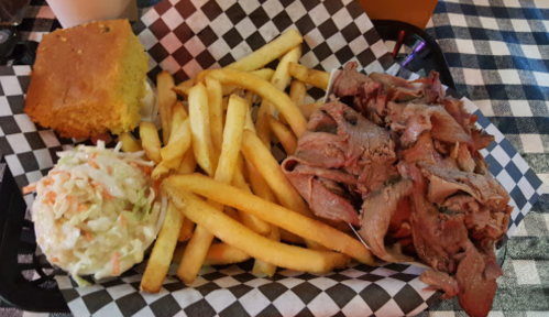 A plate with pulled pork, fries, coleslaw, and cornbread on a checkered tablecloth.