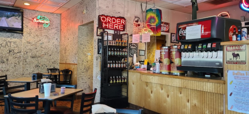 Interior of a casual restaurant with a counter, soda fountain, neon signs, and walls covered in signatures and drawings.