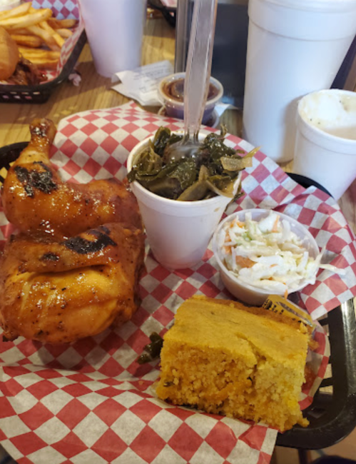 A plate featuring grilled chicken, collard greens, coleslaw, and cornbread, served in a basket with checkered paper.