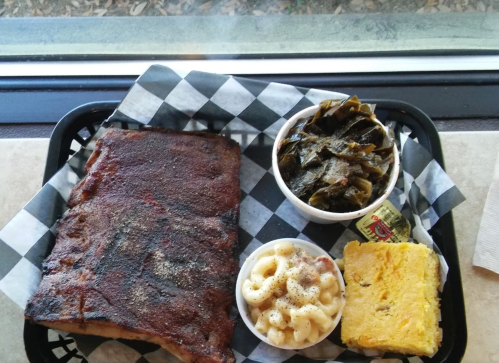 A tray with BBQ ribs, macaroni and cheese, collard greens, and cornbread, served with a small butter packet.