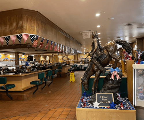 Interior of a restaurant featuring a horse statue, patriotic decorations, and a "Please Seat Yourself" sign.