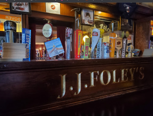 A wooden bar with the name "J.J. Foley's" and various beer taps in a cozy pub setting.