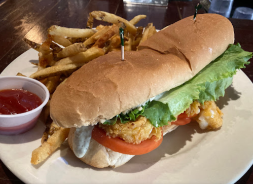 A sandwich with fried fish, lettuce, and tomato, served with a side of fries and a small cup of ketchup.