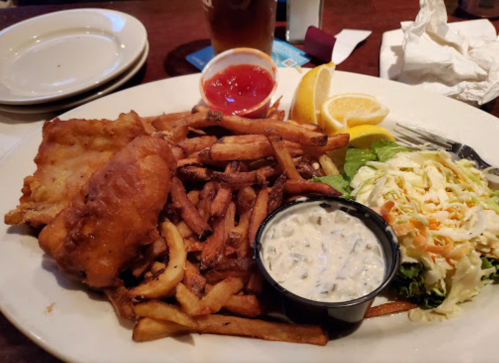 A plate of fried fish, French fries, coleslaw, and dipping sauce, garnished with lemon wedges.
