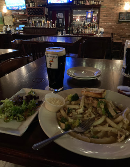 A plate of pasta with broccoli, a side salad, and a pint of Guinness on a wooden table in a bar setting.