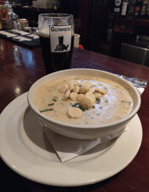 A bowl of creamy soup topped with crackers, alongside a pint of Guinness beer on a wooden bar.
