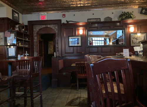 Cozy restaurant interior with wooden furniture, mirrors, and a warm ambiance, featuring a bar and empty tables.