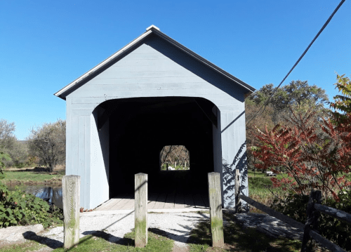 A blue covered bridge with a wooden walkway, surrounded by trees and a clear blue sky.