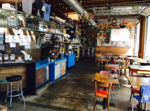 A cozy restaurant interior with wooden tables, colorful chairs, and a vibrant decor of posters and lights.